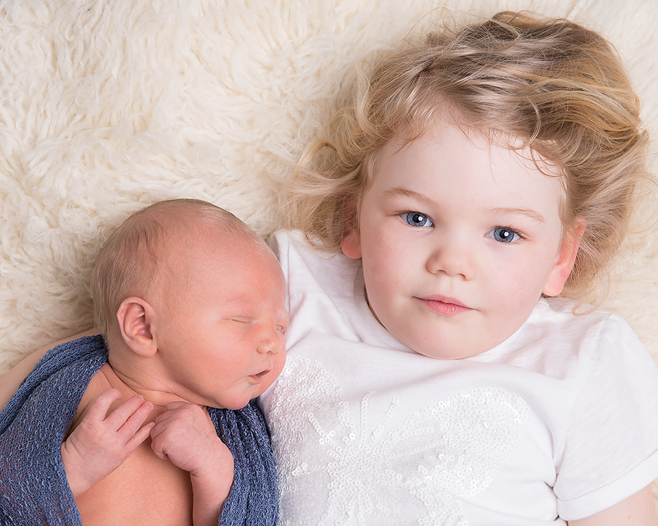 A big sister cuddles up with her newborn baby brother