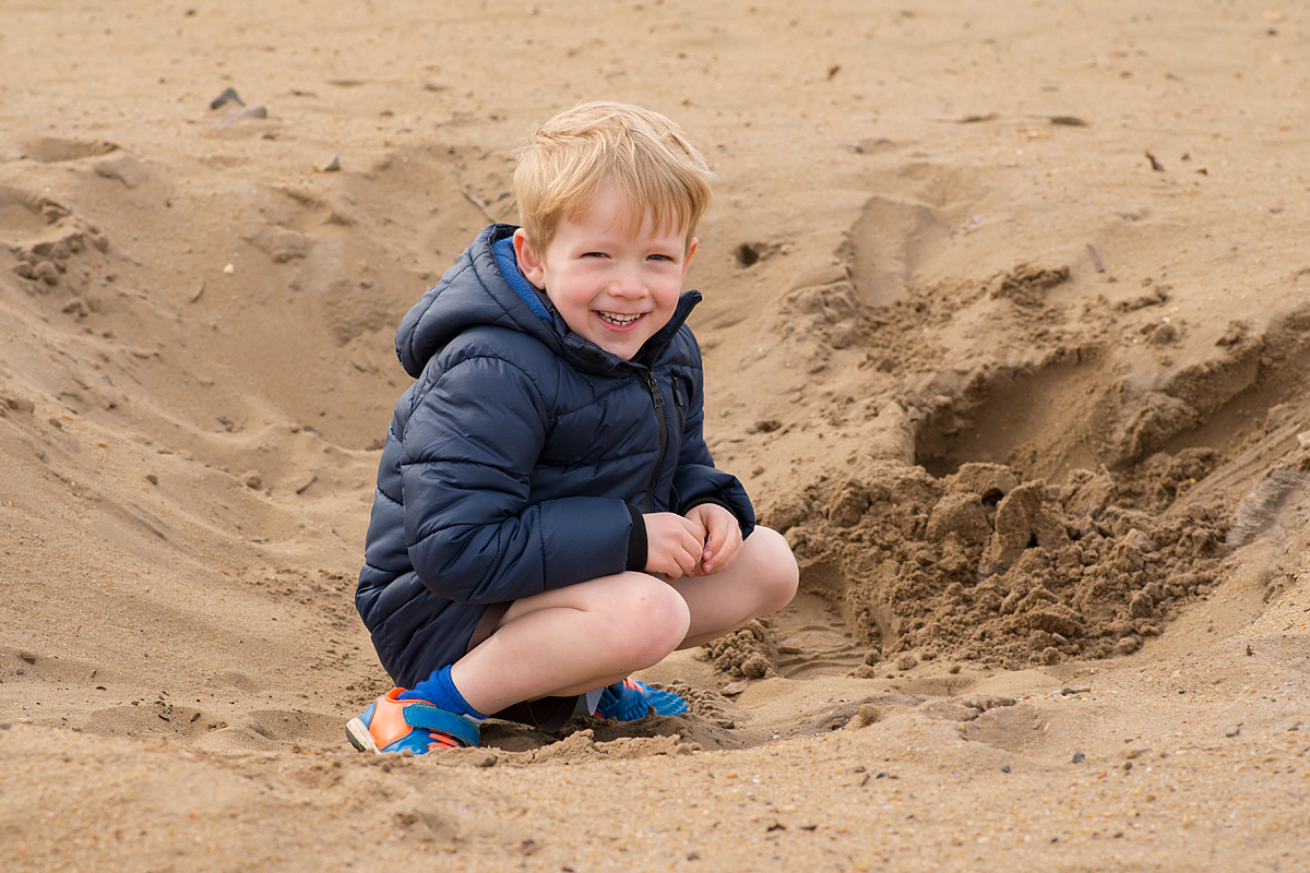Little boy crouching on the sand at Frensham Ponds