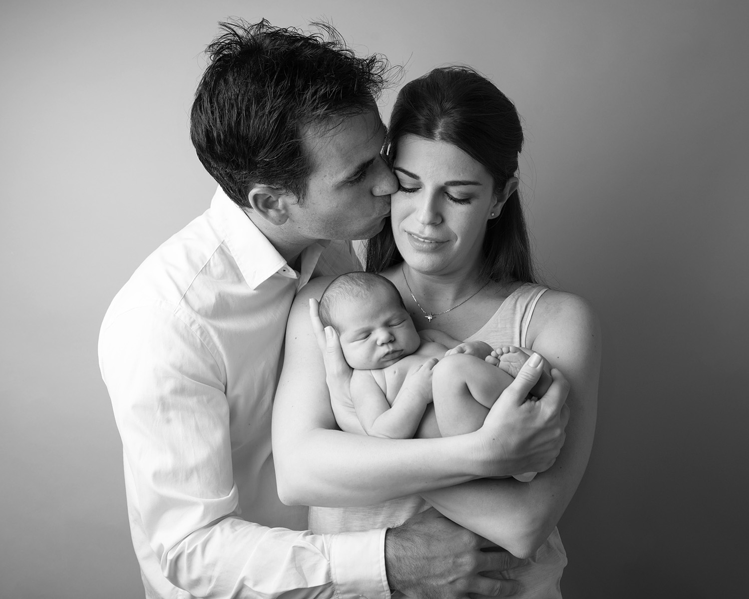 A doting father embraces his wife as she holds his baby girl